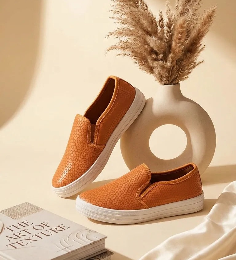 Tan perforated leather slip-ons beside a vase of dried pampas grass