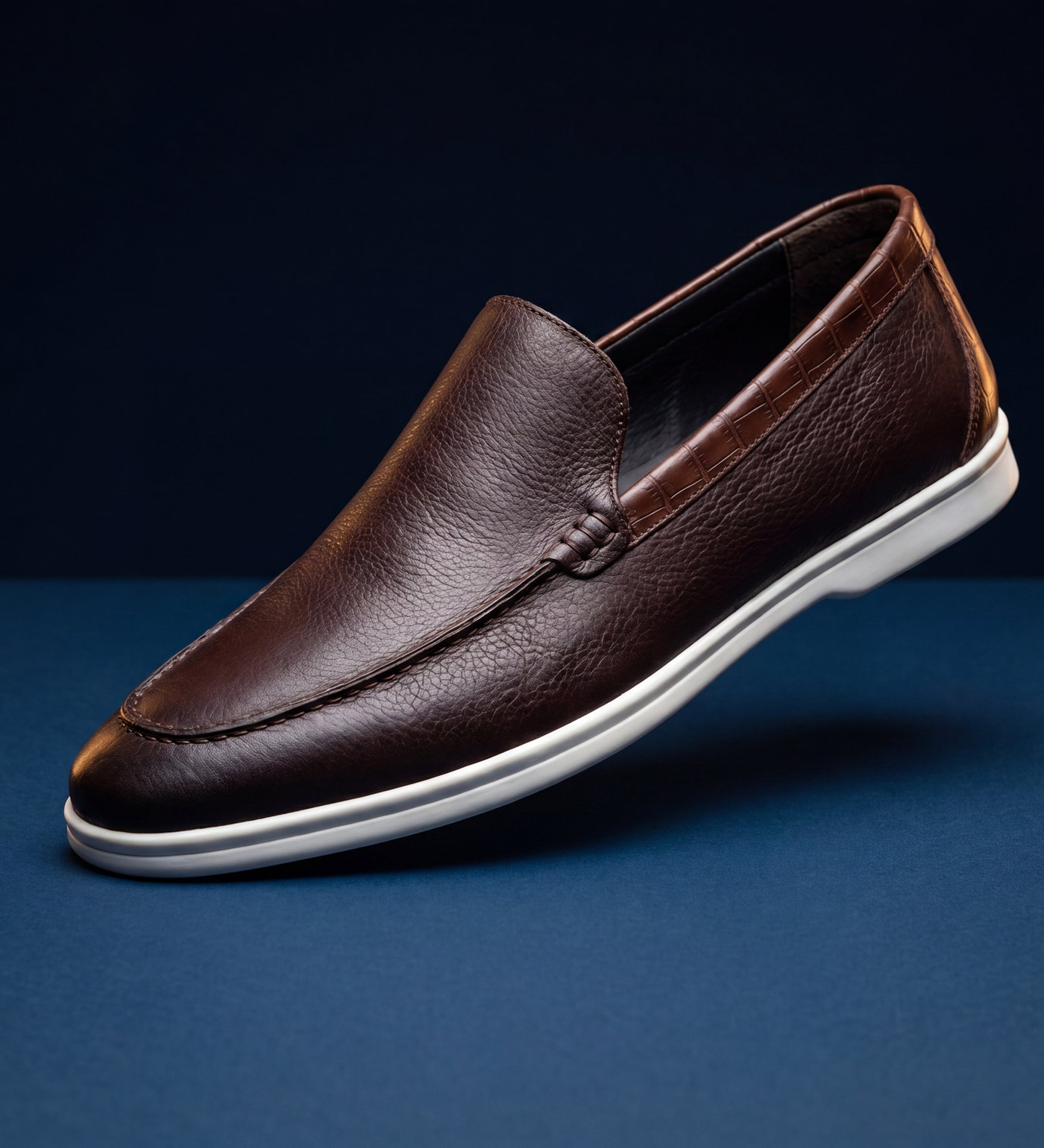 A brown leather loafer with a white sole on a navy set