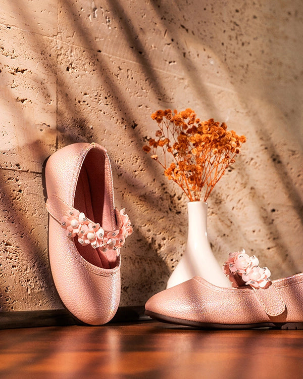 Blush ballet flats with flower straps beside a vase of dried flowers